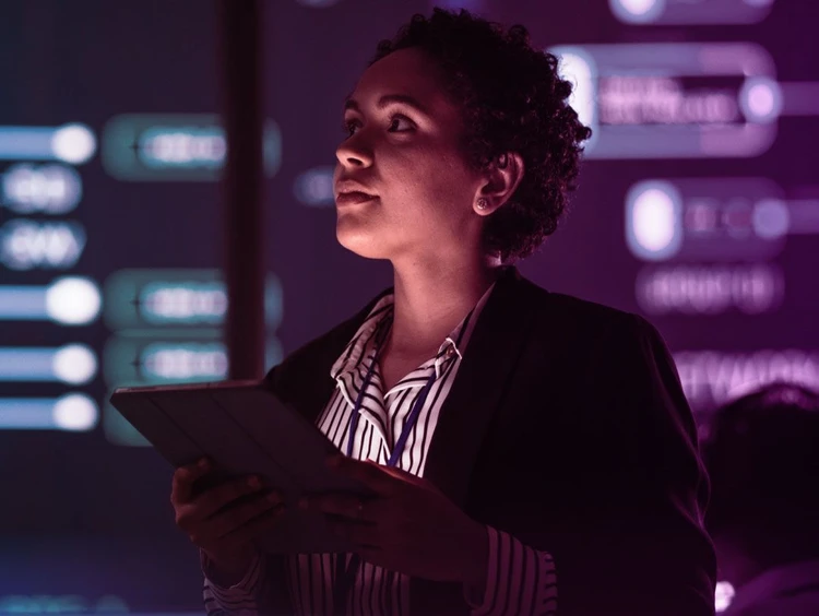 Professional looks at a virtual whiteboard with graphics while holding a tablet.