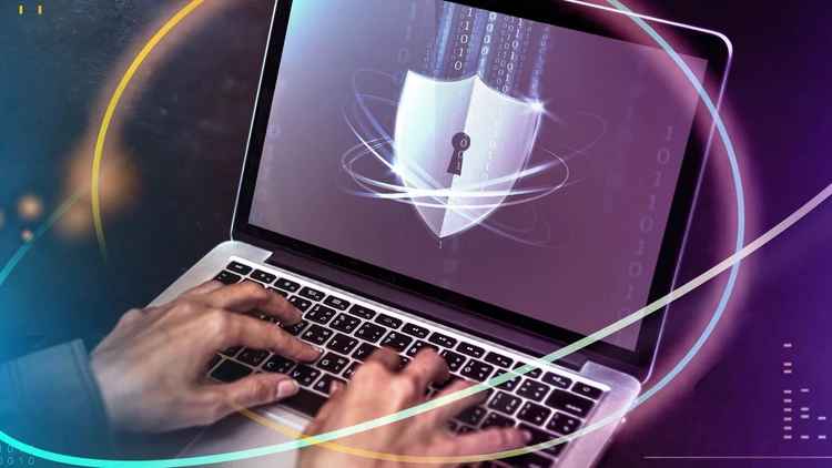 Laptop displaying a shield icon with a padlock, with hands typing on the keyboard, representing cybersecurity.